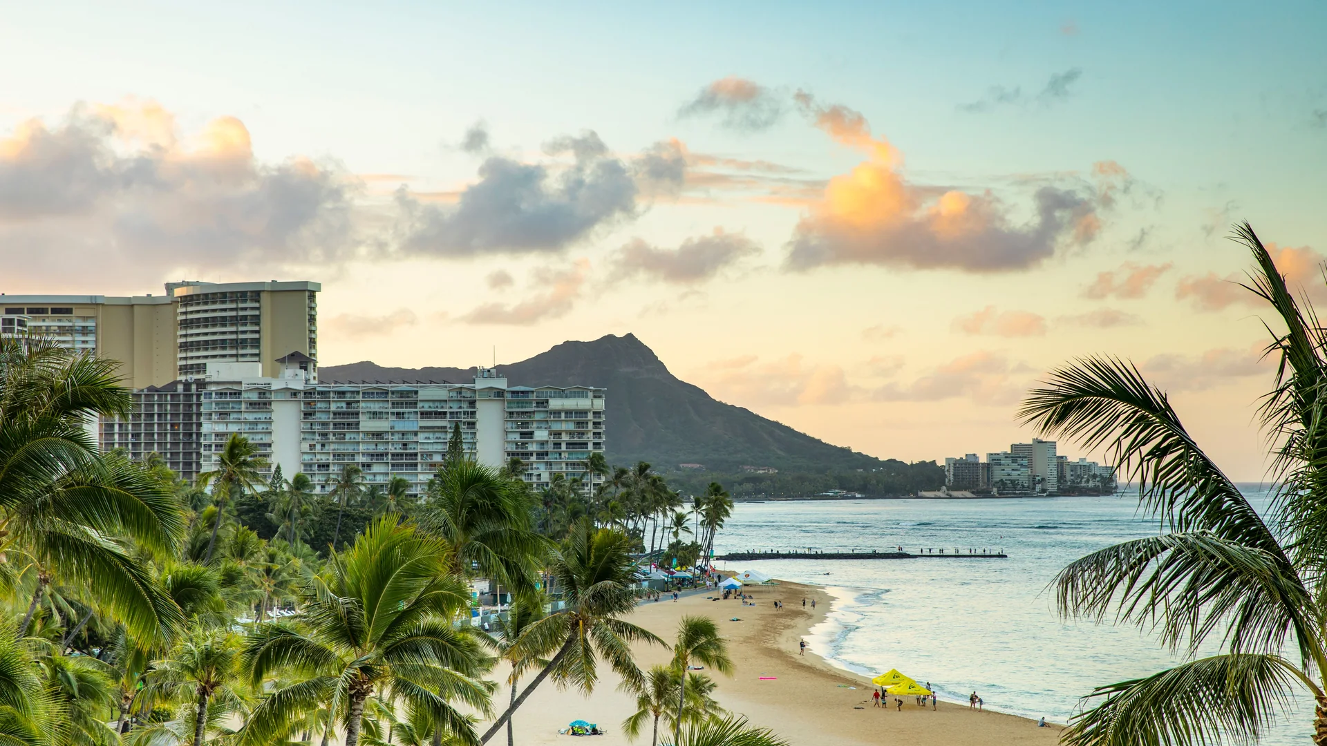 Diamond Head and the hotels of Waikiki Beach lit by a pastel sunset, framed by palm fronds