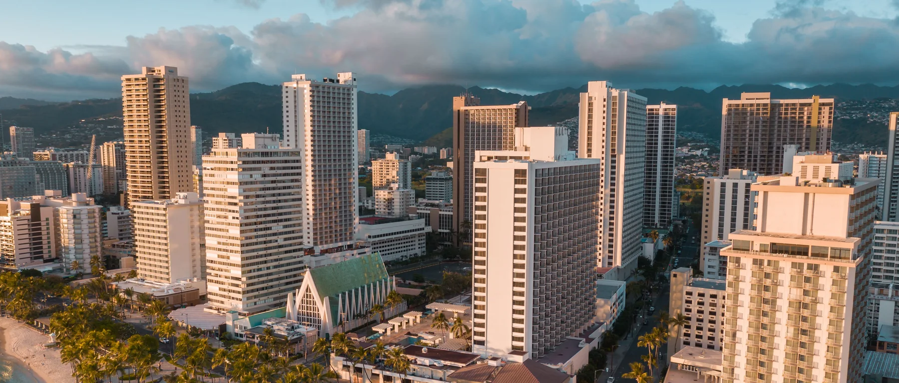 Aerial view of Waikiki's beachfront hotels and Kalākaua Avenue beside the sand at sunset